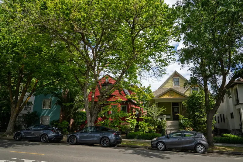 Older two-story houses in Midtown Sacramento set back behind lawns under tall street trees